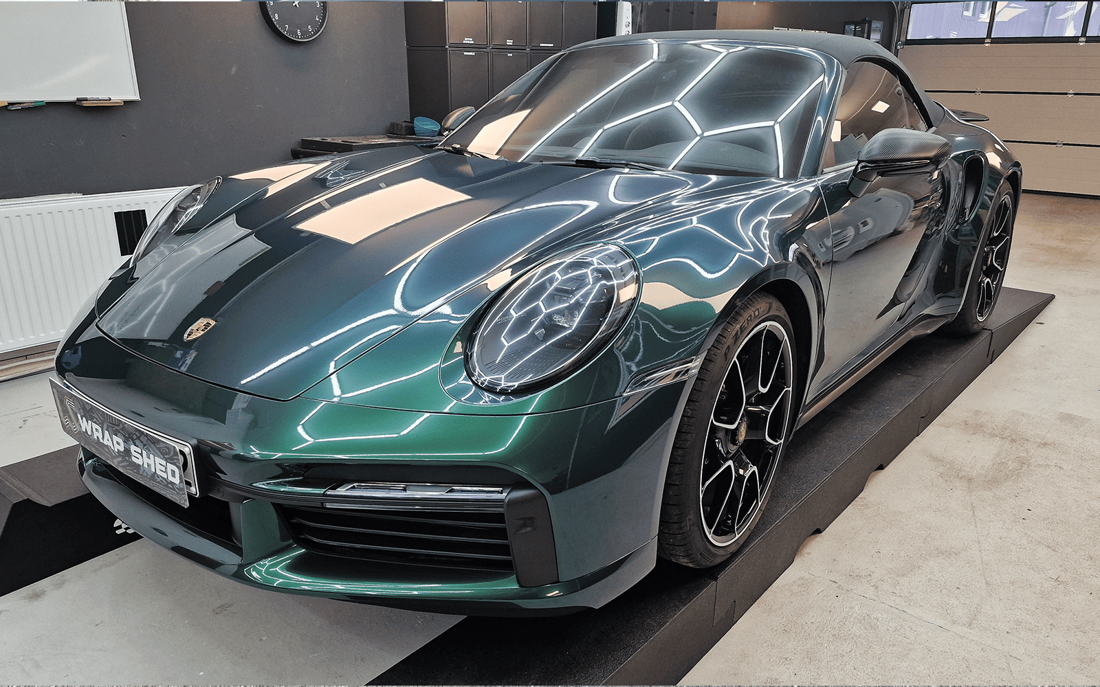 Frontansicht des grün folierten Porsche 911 unter Werkstattbeleuchtung