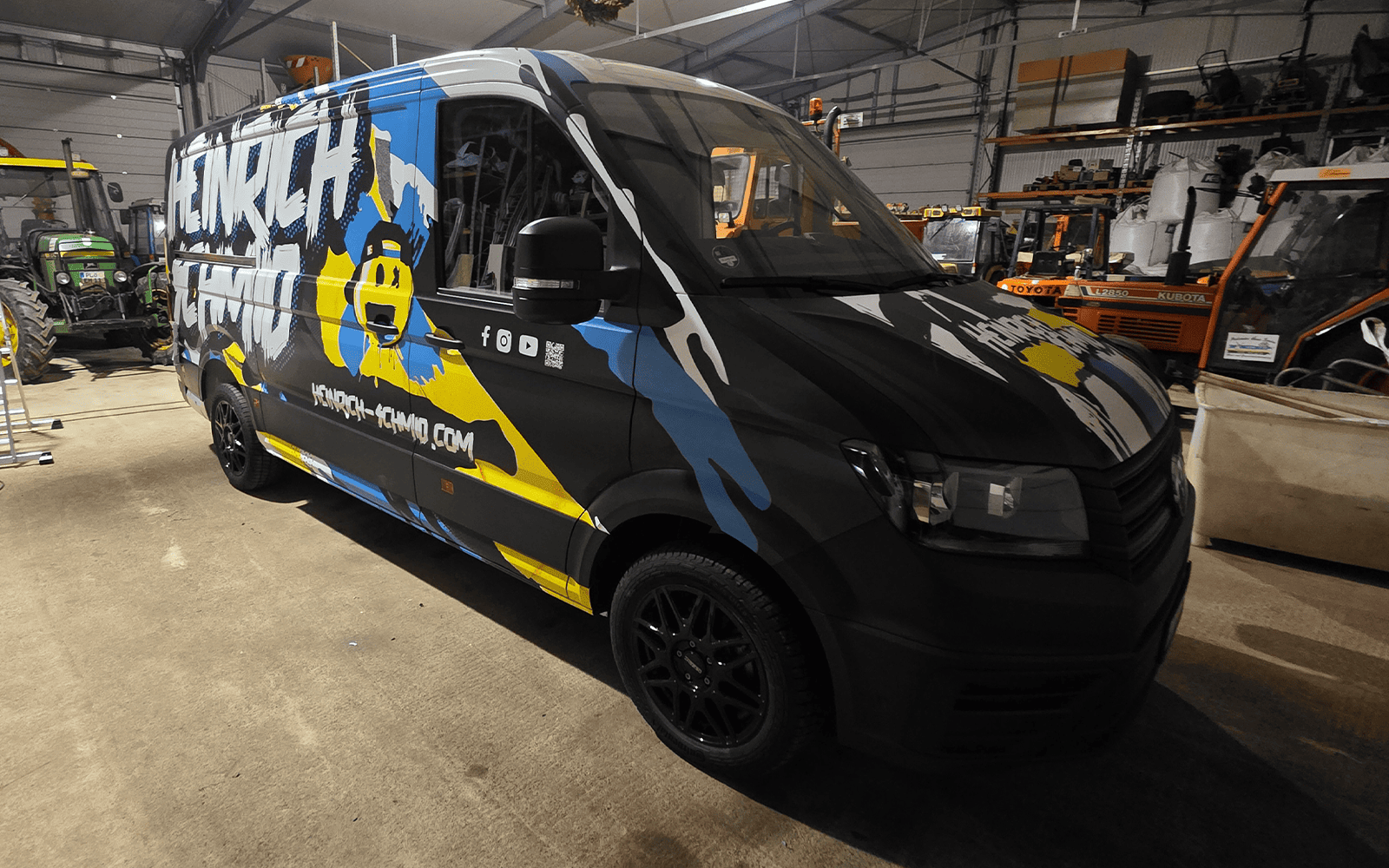 VW Transporter mit schwarz-blau-gelber Grafikfolierung in der Werkstatt