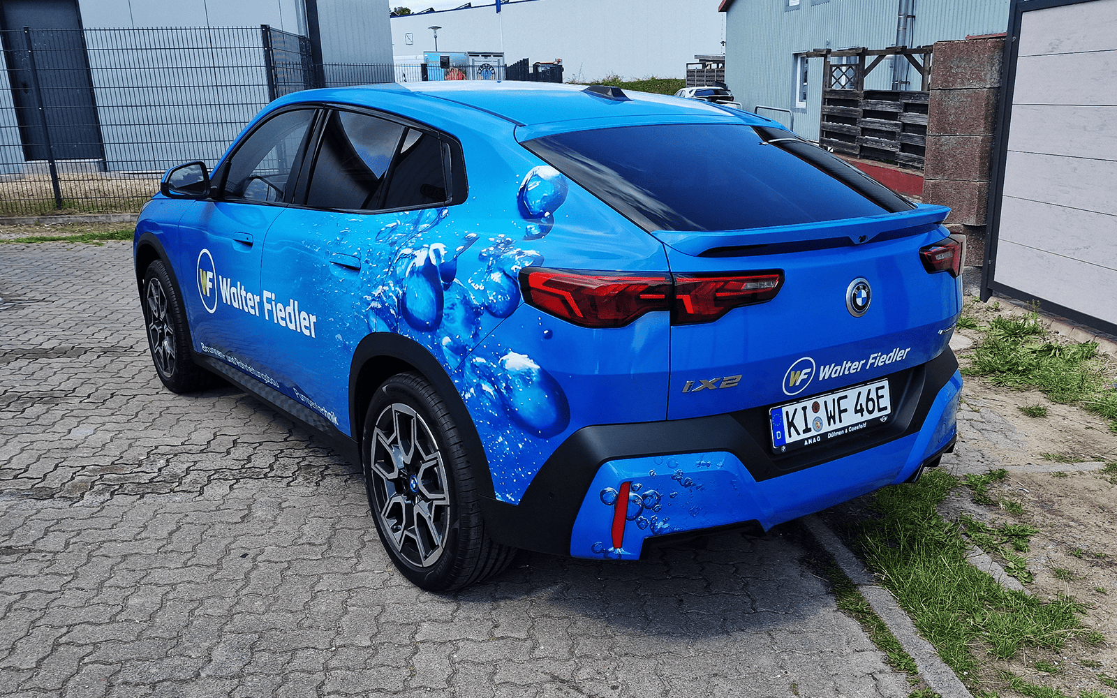 Heck des blauen BMW iX2 mit Walter-Fiedler-Beschriftung