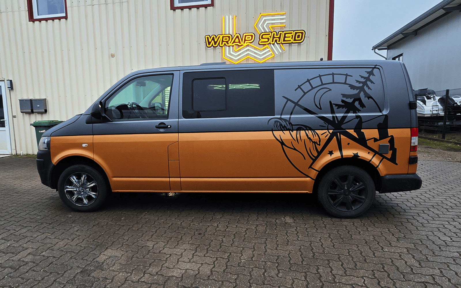 VW Transporter mit Wald-Grafik und kupferfarbener Folierung vor der Wrap-Shed-Halle